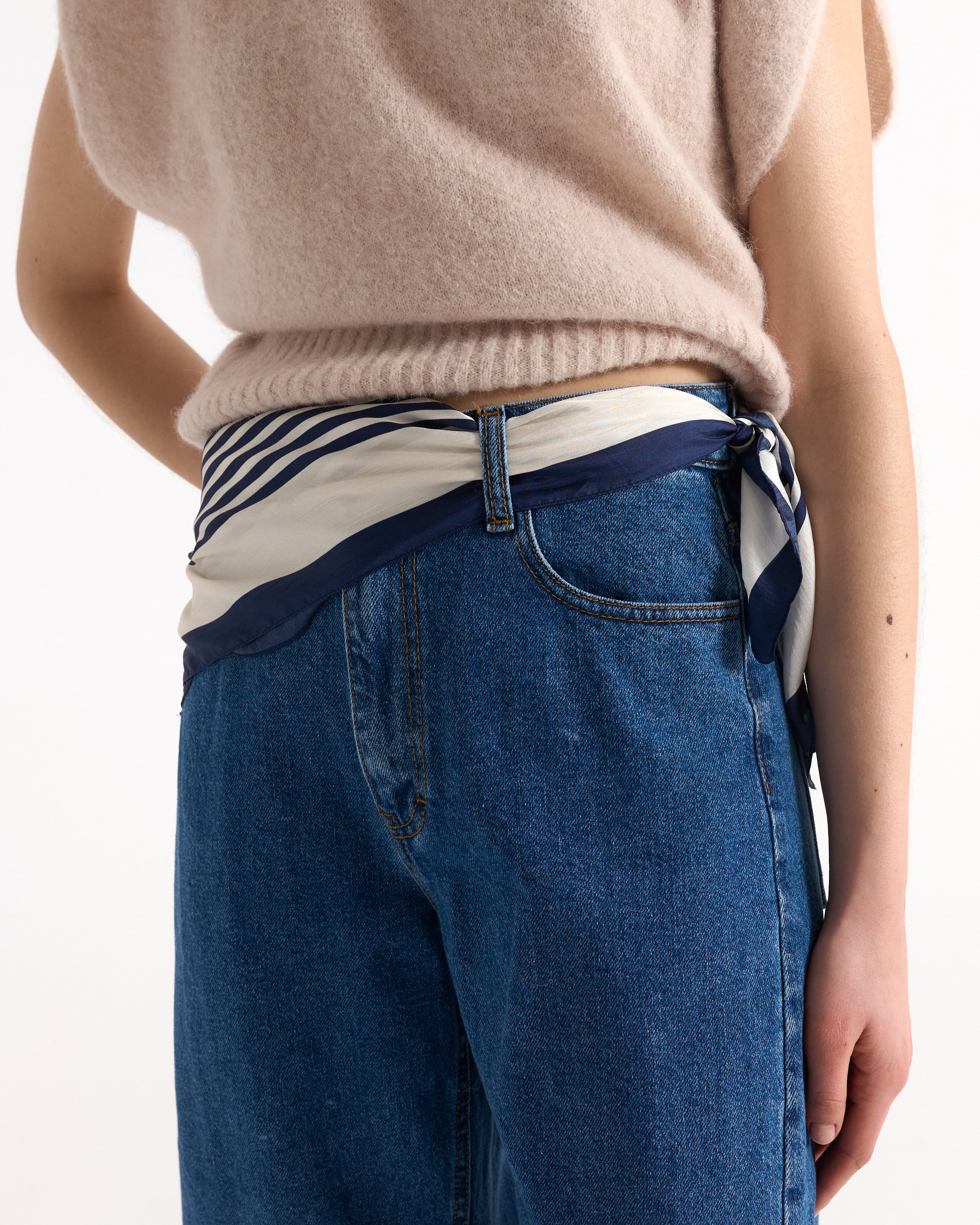 draagt blauwe spijkerbroek, blauw denim, hoog taille, sjaalriem, breisels sweater